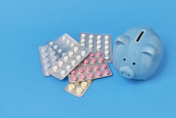 piggy bank and pills on a blue background, concept of saving on drugs, online shopping - Foto, immagini