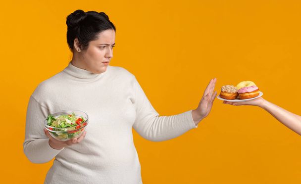 Chica regordeta rechazando comida chatarra, sosteniendo tazón con ensalada de verduras frescas
 - Foto, Imagen