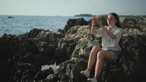 Chica disfrutando de la vista al mar y tomar fotos móviles de olas rompiendo
 - Metraje, vídeo
