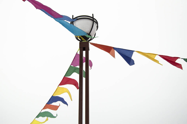Banderas triangulares festivas en forma de guirnaldas cuelgan atadas a un poste de luz. Ideas de decoración en la celebración de un evento, aislado sobre un fondo blanco
 - Foto, Imagen