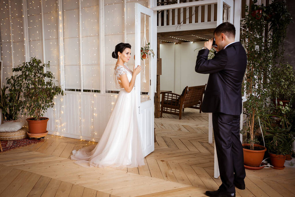 Um noivo em um terno fotografa uma noiva bonita em um dr elegante
 - Foto, Imagem