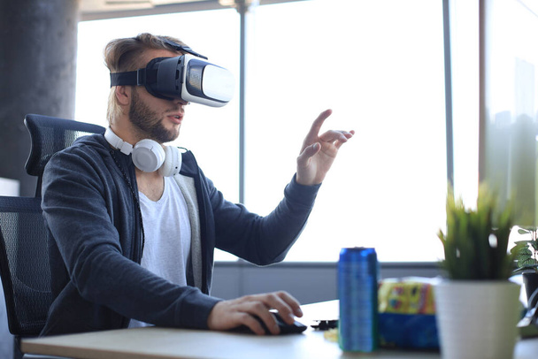 Young bearded man wearing virtual reality glasses in modern interior design coworking studio. - Фото, изображение