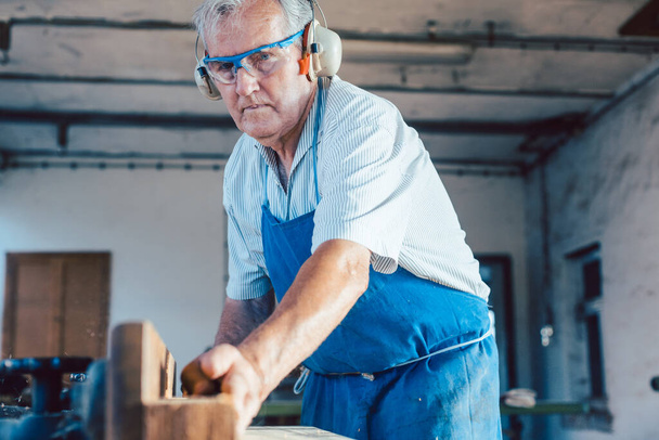 Menuisier senior travaillant avec raboteuse à bois sur pièce - Photo, image
