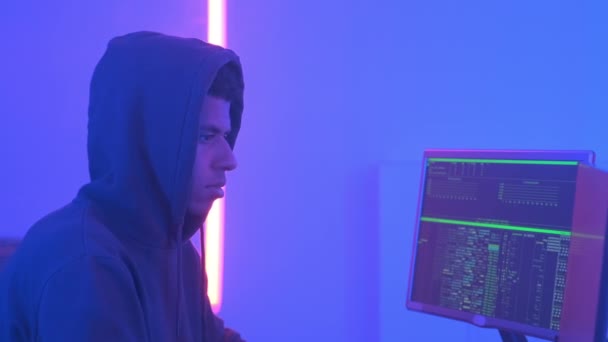 Ekran ekranlarıyla dolu bir odada çalışan Afrikalı kapüşonlu hacker profili - Video, Çekim