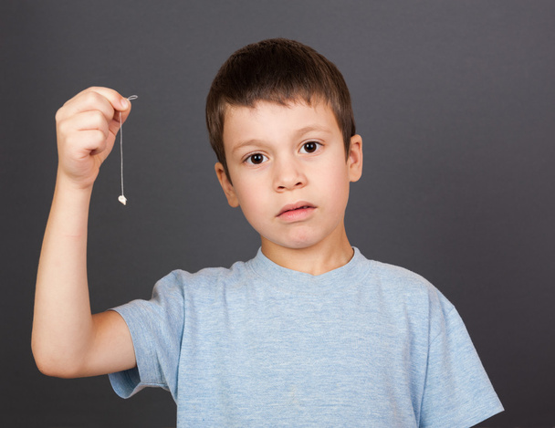 сумний хлопчик показує втрачений зуб на нитці
 - Фото, зображення