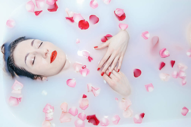 Young sexy girl taking a milk bath with rose petals closeup - Photo, Image
