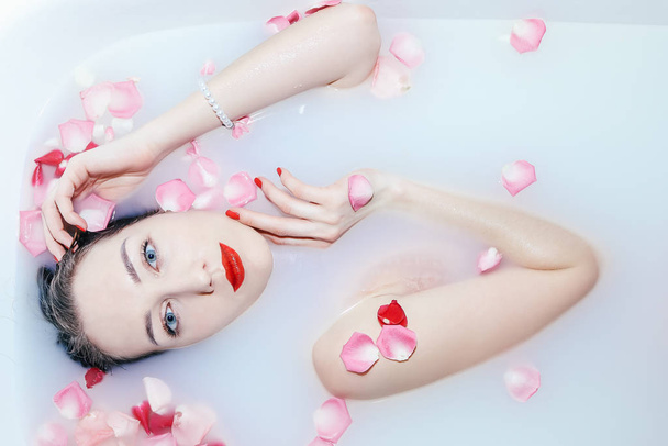 Young sexy girl taking a milk bath with rose petals closeup - 写真・画像