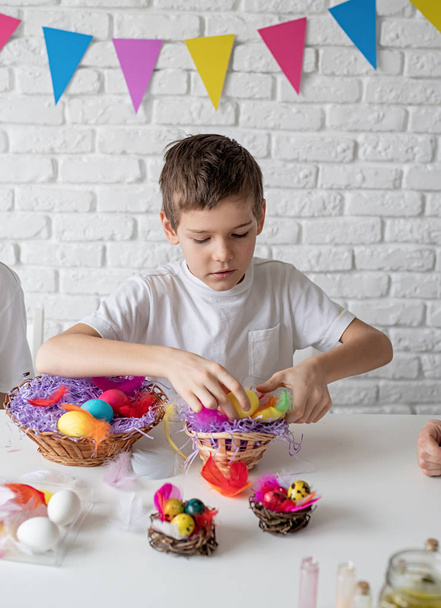 Happy boy versieren een nest met gekleurde eieren voor Pasen - Foto, afbeelding
