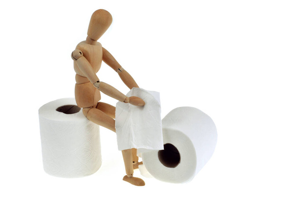 Concept de constipation avec un mannequin en bois assis sur un rouleau de papier toilette gros plan sur fond blanc
 - Photo, image