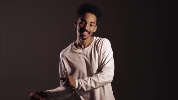 Joven hombre afroamericano enérgico en blanco llevar sonriendo y bailando de buen humor, chasquea los dedos sobre fondo marrón. 4k
 - Imágenes, Vídeo