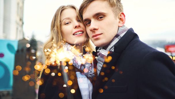 retrato do casal romântico elegante sorrindo para a câmera, com brilho nas mãos no fundo decorações da cidade festiva. - Foto, Imagem