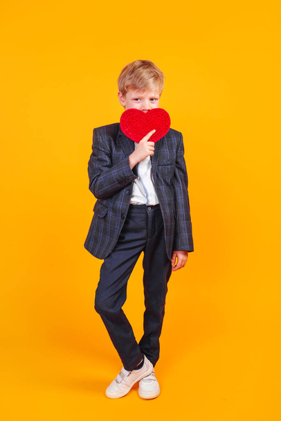 Little cheerful boy in love holding red heart over eyes and smiling - Foto, afbeelding