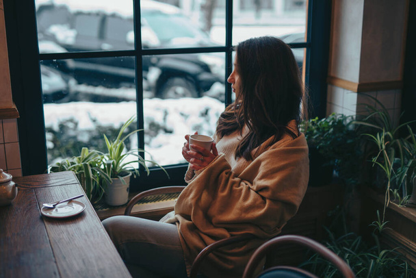 Young woman drinking tea in cafe looking through window - Φωτογραφία, εικόνα