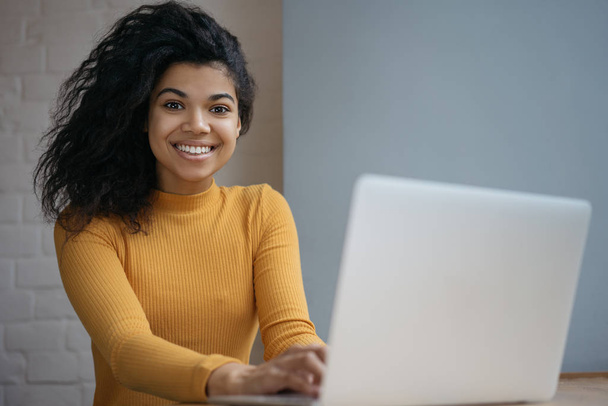 Mulher de negócios afro-americana bonita usando computador portátil, sentado no escritório. Retrato do projeto de trabalho de redator freelancer bem sucedido no local de trabalho. Língua de aprendizagem do estudante online
   - Foto, Imagem