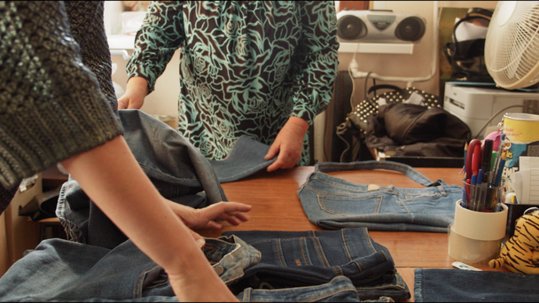 naisten räätälit työskentelevät vanhojen farkkujen osien kanssa suuressa pöydässä
 - Materiaali, video