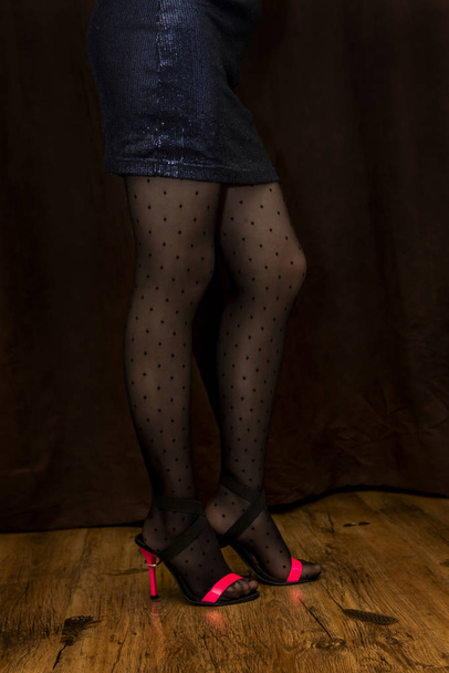 Slanke benen van meisje in modieuze zwarte panty met zwarte stippen en hoge hakken - Foto, afbeelding