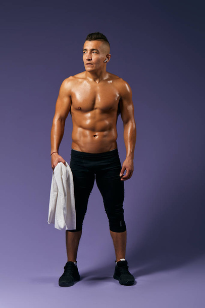 sporty muscular man holding a white towel on blue background. - Фото, зображення