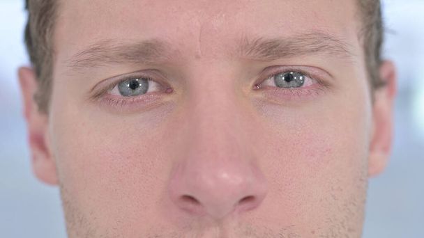 close-up van knipperende ogen van jonge man op zoek naar camera  - Foto, afbeelding
