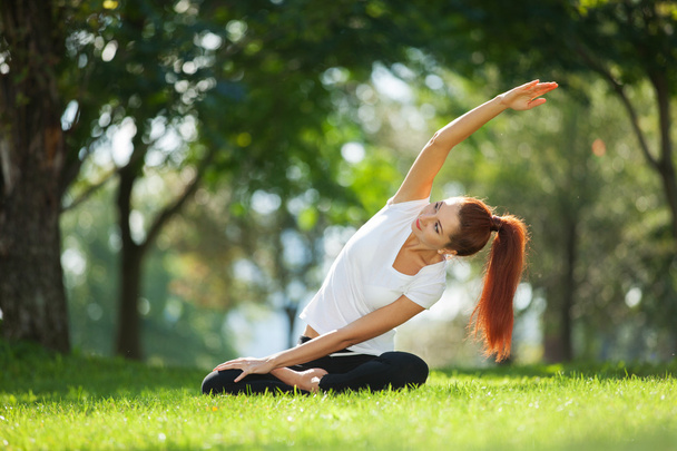 Pretty woman doing yoga exercises in the park - 写真・画像
