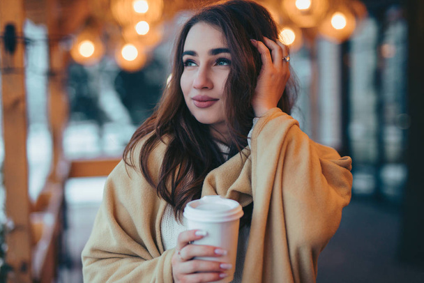 Mulher bonita segurando xícara de café de papel no terraço do café no dia de inverno
 - Foto, Imagem