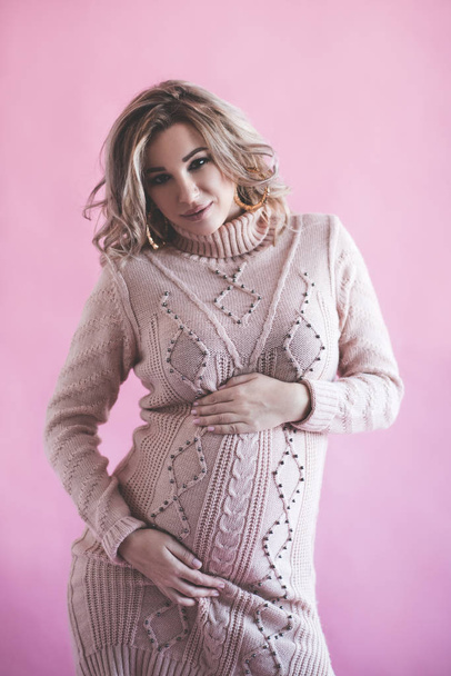 stylische schwangere Frau in Strickkleid posiert vor rosa Hintergrund. Mutterschaft. Mutterschaft. Gesundheitsversorgung.  - Foto, Bild