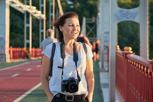 Mature female with backpack photo camera smiling on sunny summer day - Fotó, kép
