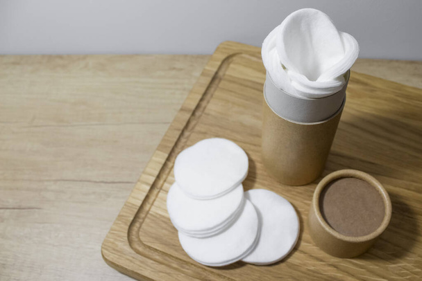 Paper tube with white cotton pads or rounds inside on wooden board. Recycle concept showing how to reuse cardboard packaging for natural cosmetics at home. Top view with copy space - Photo, Image