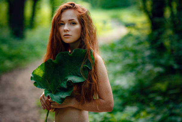 Молодая рыжая женщина стоит в зеленом лесу
. - Фото, изображение
