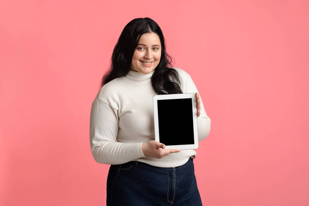 Donna grassoccia sorridente che dimostra la compressa digitale con schermo nero vuoto
 - Foto, immagini