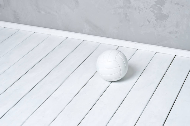Білий волейбол лежить на дерев'яній поверхні біля сірої стіни з копіювальним простором
 - Фото, зображення