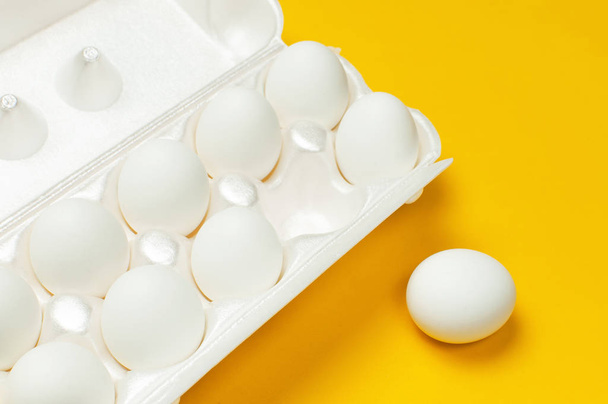Белые куриные яйца в белой упаковке на желтом фоне сверху плоского вида лежат в копировальном пространстве. Яйца в коробке, натуральная здоровая пища и органическое земледелие. Креативные продукты питания минималистский фон, Пасха
 - Фото, изображение