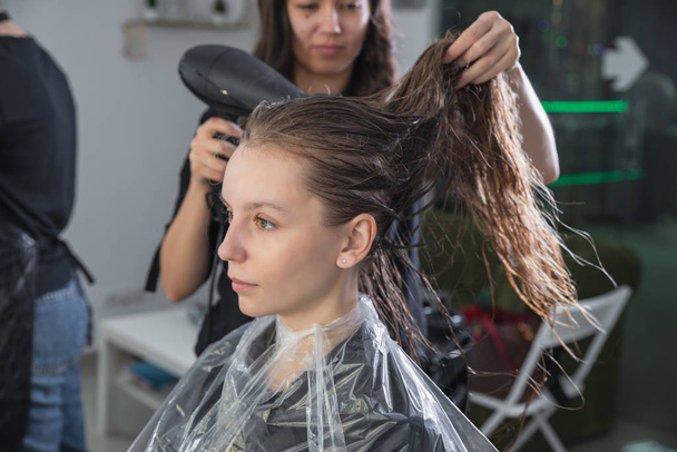 Primer plano de peluqueros manos secado pelo largo y rubio con secador de pelo y cepillo redondo
 - Foto, Imagen
