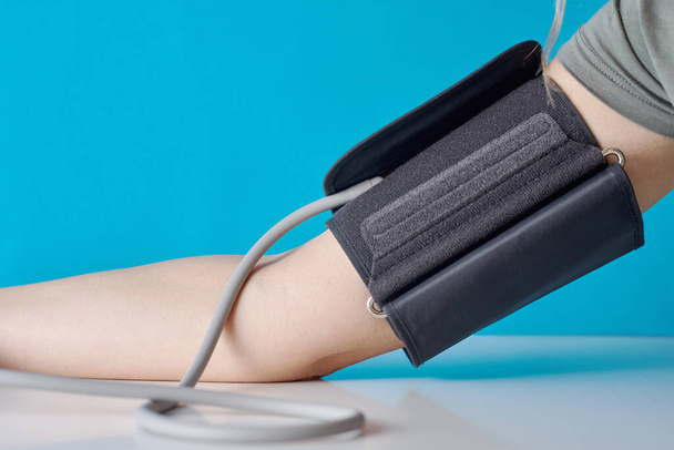 Kobieta mierzy ciśnienie krwi cyfrowym monitorem ciśnienia na niebieskim tle. Opieka zdrowotna i koncepcja medyczna - Zdjęcie, obraz