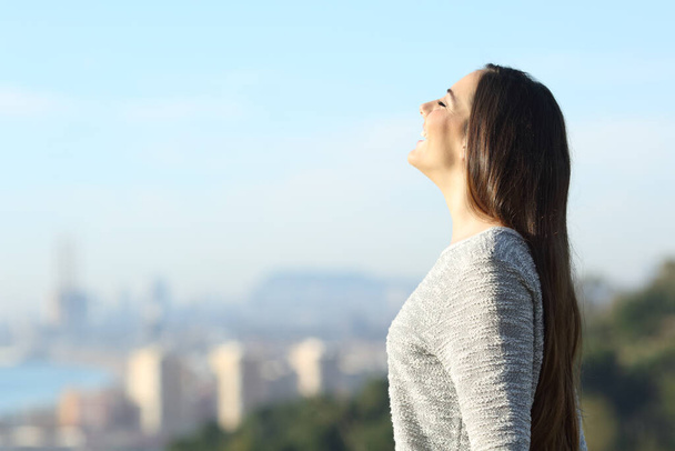 Happy woman breathing fresh air with a city in the background - Φωτογραφία, εικόνα