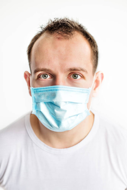 Vertical close-up portrait of scared caucasian man in blue medical mask on face, afraid of coronavirus. Health care in cold season. Scared expression - Photo, Image
