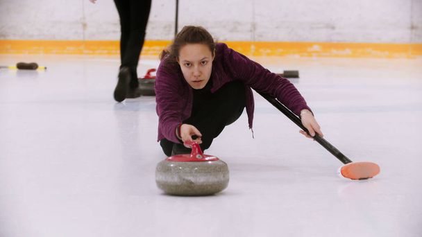 Curling - une femme patinant sur un champ de glace avec une pierre de granit tenant une brosse
 - Photo, image