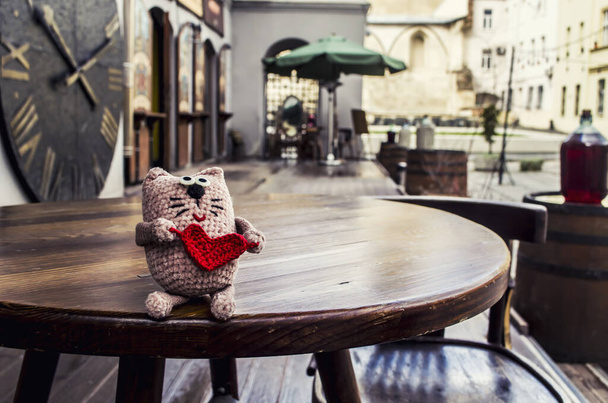 旧市街の背景に赤いハートの愛らしいかぎ針編みの猫. - 写真・画像