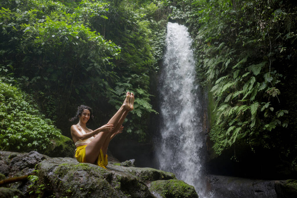 young attractive and happy hipster woman doing yoga outdoors at beautiful tropical waterfall meditating enjoying freedom and nature in healthy and zen lifestyle - Foto, immagini