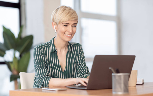 Mature Lady Working On Laptop In Earphones Sitting In Office - Photo, Image