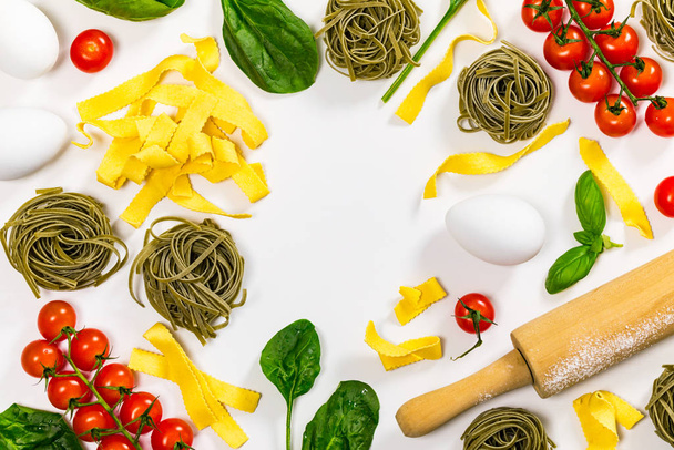 Spinach and Basil Pasta Nests, Ribbon Pasta Noodles with Tomatoes and Ingredients for Cooking Pasta on White Wooden Background, Italian cuisine, Top view. Selective focus. - Photo, Image