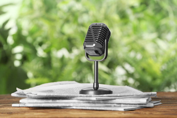 Newspapers and vintage microphone on wooden table against blurred green background. Journalist's work - Fotografie, Obrázek