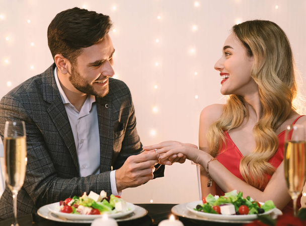 szczęśliwy mężczyzna zakładając pierścionek zaręczynowy na ręce dziewczyny na romantyczną kolację - Zdjęcie, obraz