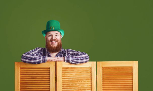 Happy Patricks Day. Funny fat bearded man in a green hat is laughing on a green background. - Photo, Image