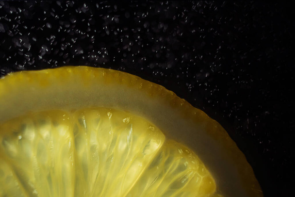 Juicy slice of lemon on a dark background. In the frame, only part of the citrus. Drops of water in the air. Detailed macro photo. Copyspace, minimalism. - Foto, afbeelding