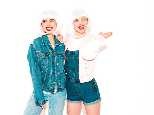 Two young sexy smiling hipster girls in white wigs and red lips.Beautiful trendy women in summer jeans clothes.Carefree models isolated on white in studio.Positive female going crazy - Photo, Image