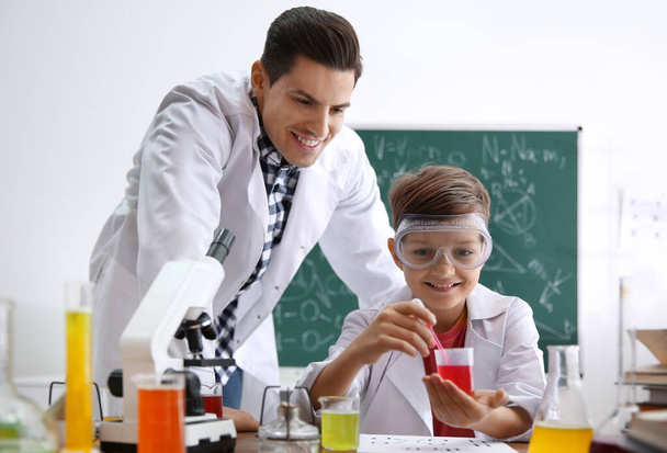 Teacher with pupil making experiment at table in chemistry class - Photo, image