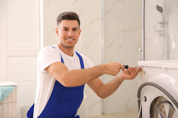 Professional plumber repairing washing machine in bathroom - Fotó, kép
