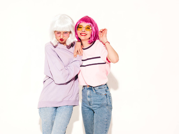 Two young sexy smiling hipster girls in wigs and red lips.Beautiful trendy women in summer clothes.Carefree models posing near white wall in studio.Positive female going crazy and hugging - Fotoğraf, Görsel