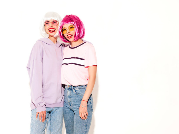 Two young sexy smiling hipster girls in wigs and red lips.Beautiful trendy women in summer clothes.Carefree models posing near white wall in studio.Positive female going crazy and hugging - Foto, immagini
