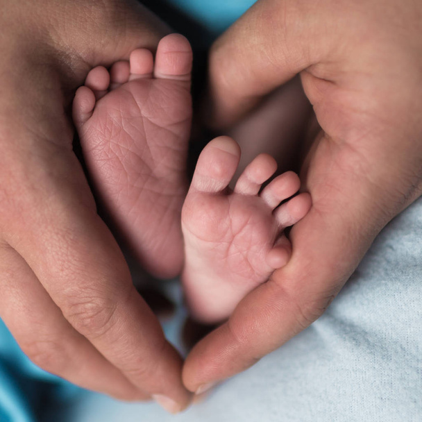 feet of a newborn child in the hands of parents. Parental care, parental love - Foto, afbeelding